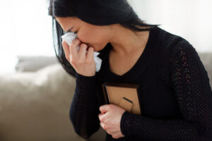 Crying woman with photo frame and paper wipe at funeral